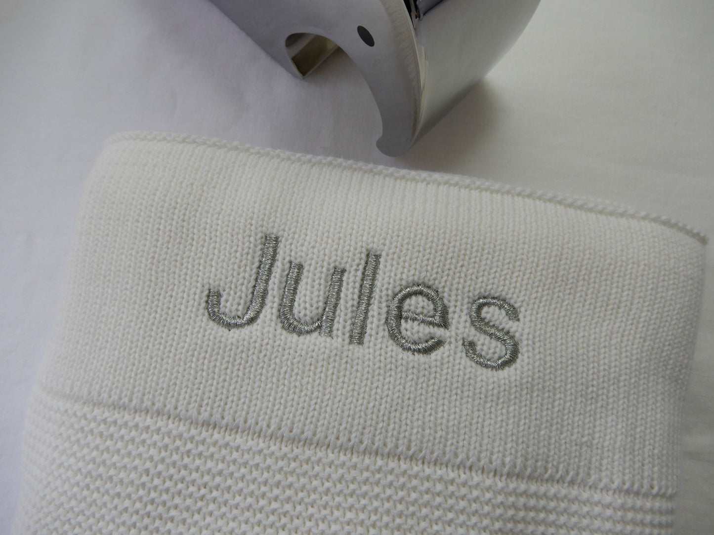 White knit baby blanket with sliver thread in bold font shown.