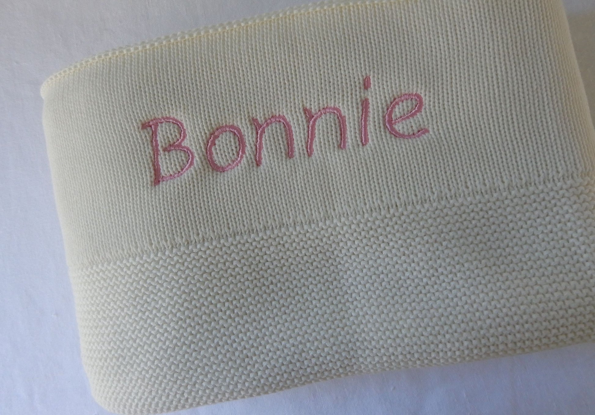 White knitted baby blanket. Personalisation with pink thread in Italic.