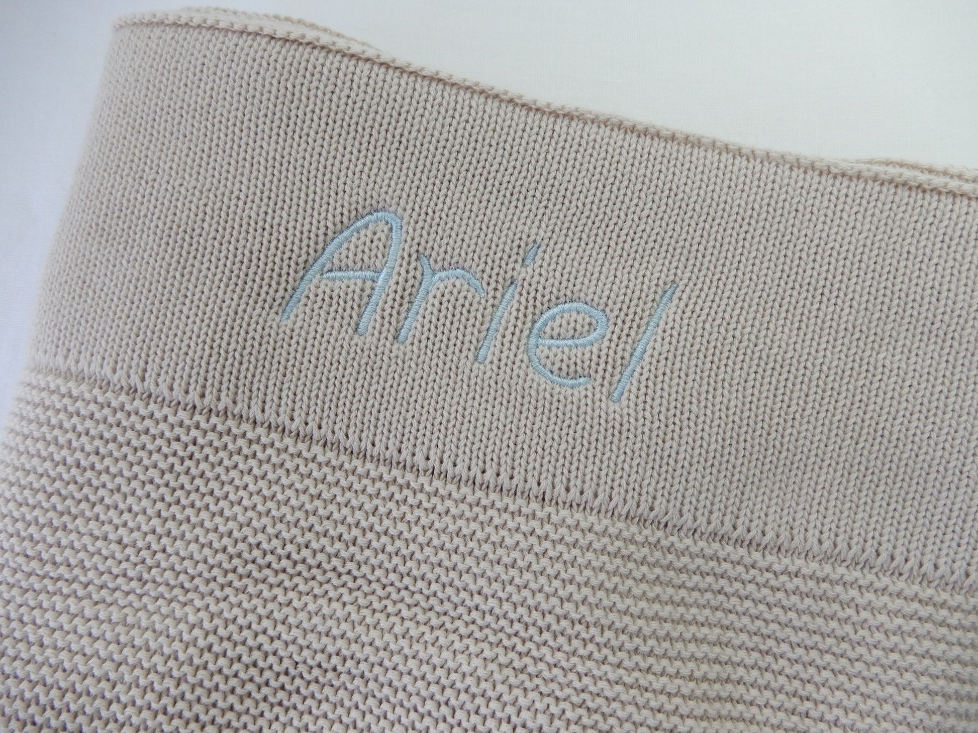 Stone baby knit blanket, personalised with light blue thread and italic font. 