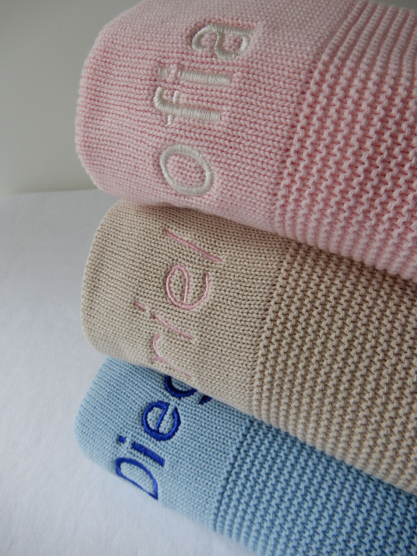 Blue, stone and pink knit blankets with variety of thread colours and text type. 