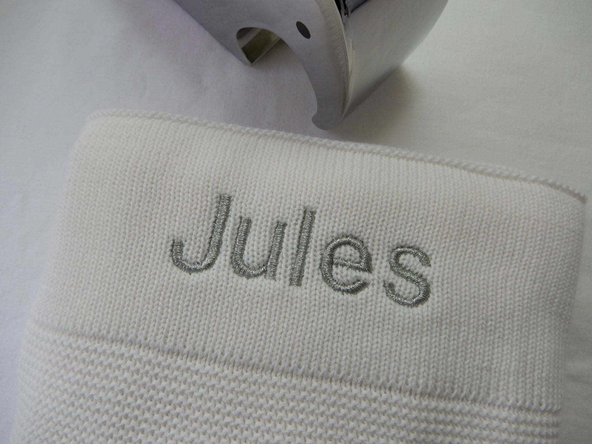 White knit baby blanket with sliver thread in bold font shown. 